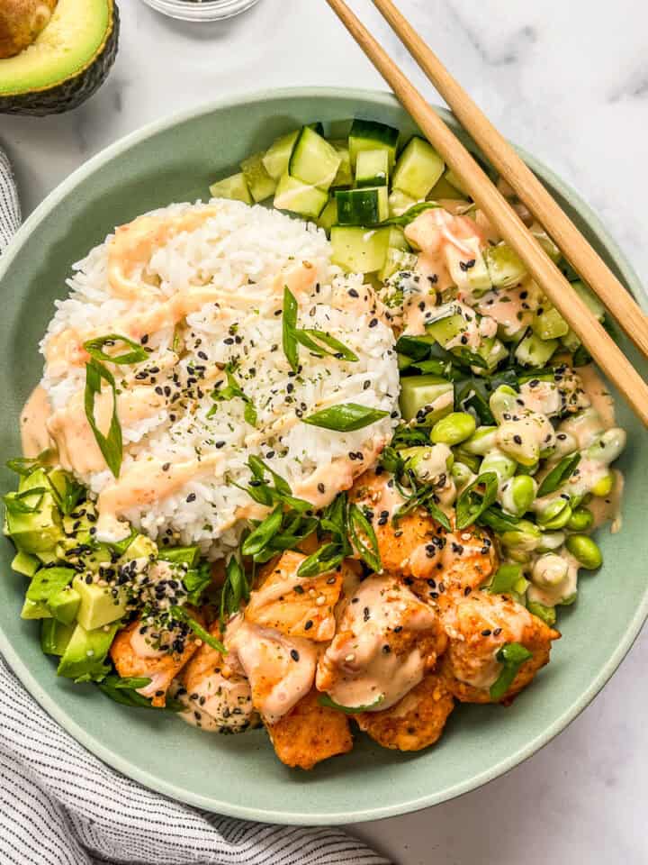 Bang bang salmon and rice bowl with veggies with chopsticks.