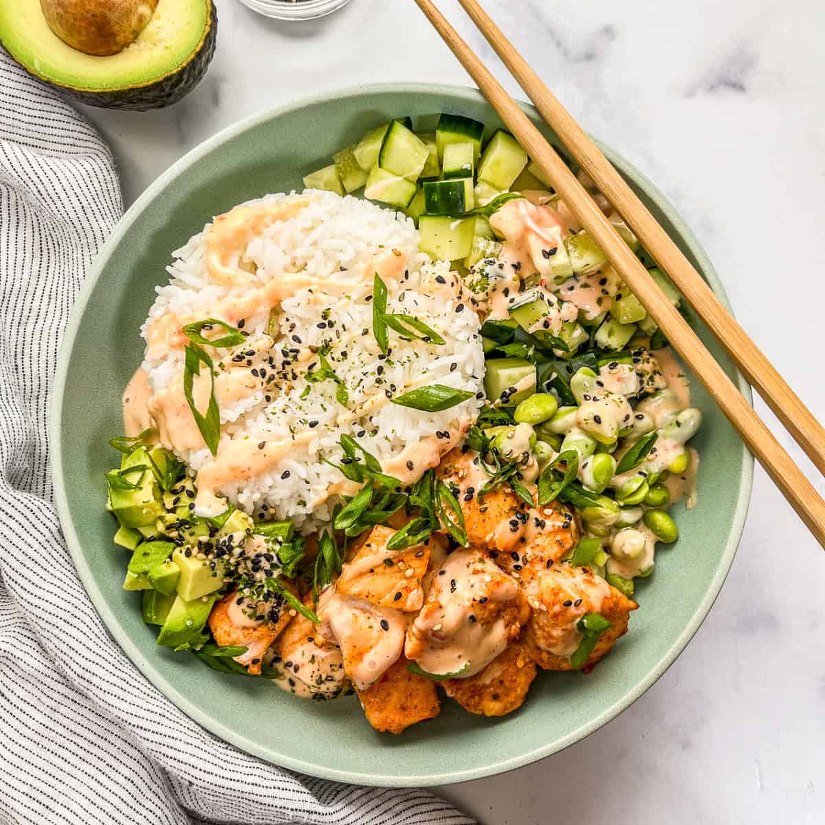 Bang bang salmon and rice bowl with veggies with chopsticks.