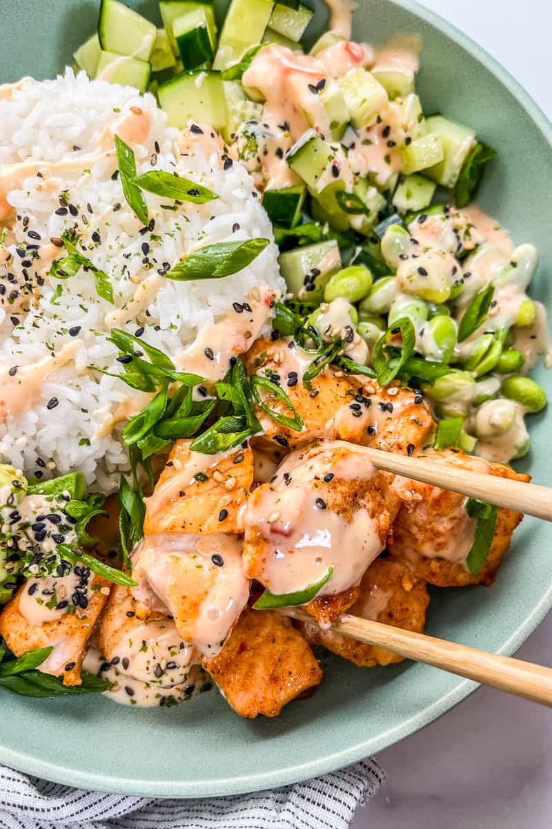 Chopsticks picking up a piece of bang bang salmon.