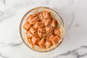 Raw salmon chunks tossed with bang bang sauce in a glass bowl.