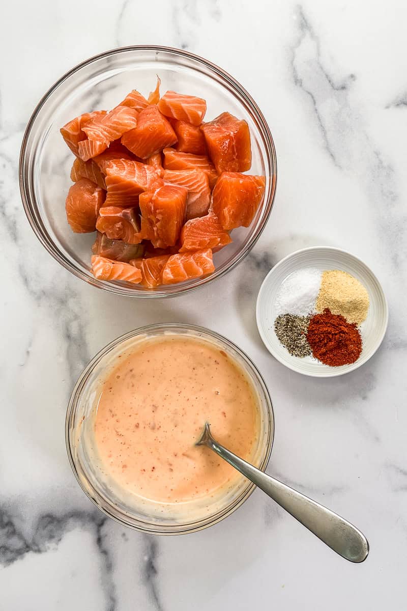 Chunks of salmon, spices, and bang bang sauce in bowls.
