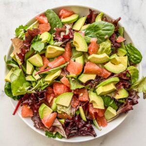 Greens, avocado, and grapefruit combined in a bowl.