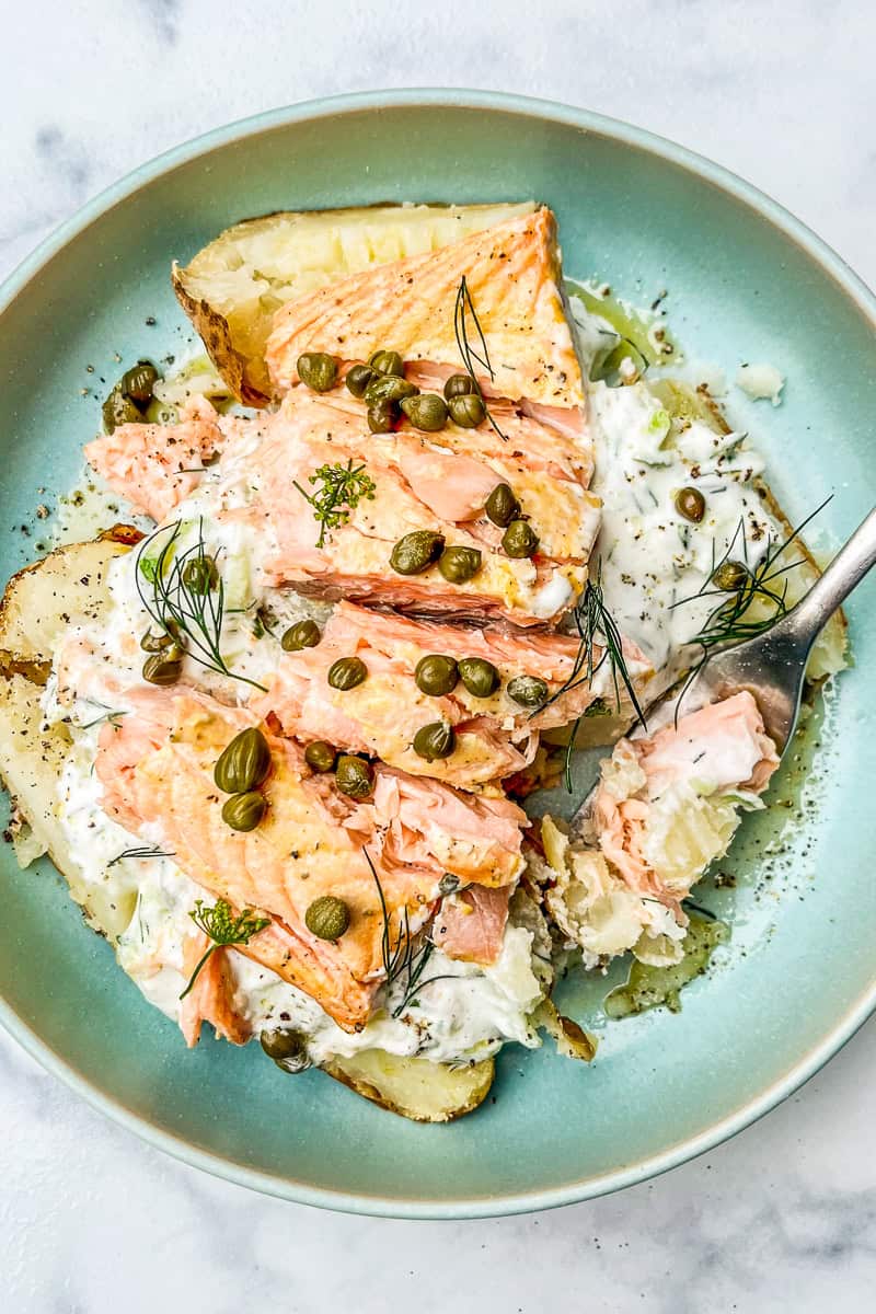 Baked potato topped with dill sauce, salmon, and capers.