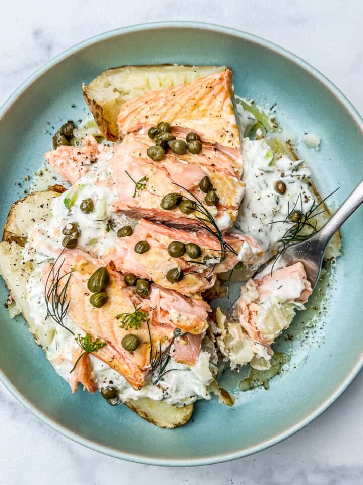 Salmon baked potato with dill sauce in a blue bowl.