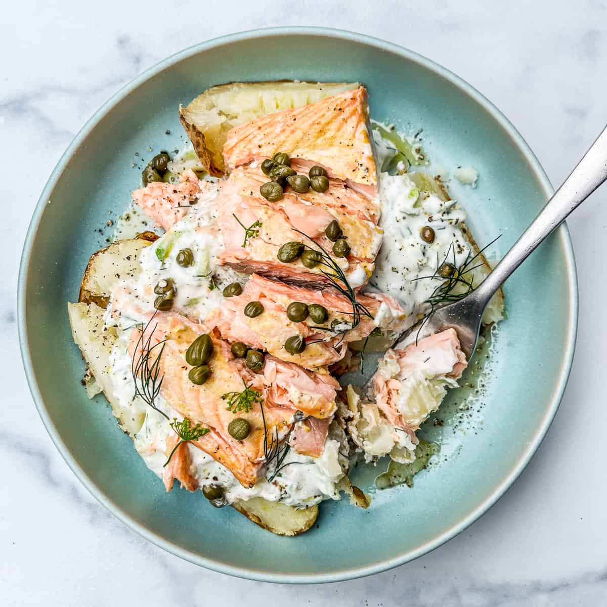 Salmon baked potato with dill sauce in a blue bowl.