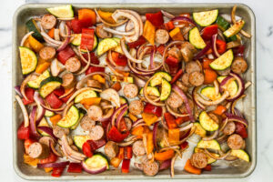 Baked sausage with veggies on a silver sheet pan.