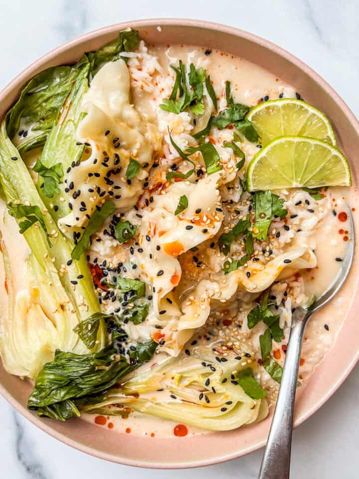 Coconut curry dumpling soup with bok choy in a pink bowl with a silver spoon.