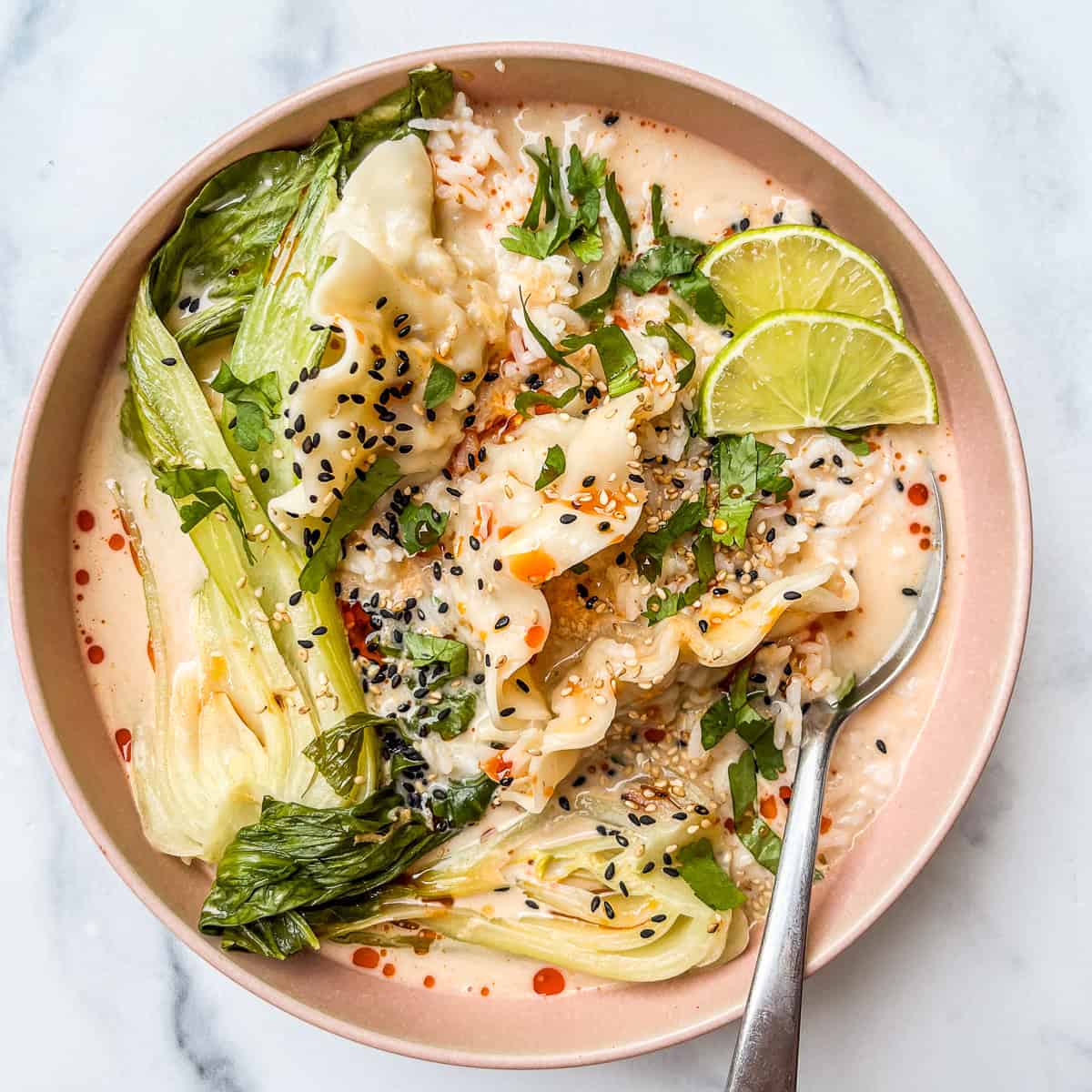 Coconut curry dumpling soup with bok choy in a pink bowl with a silver spoon.