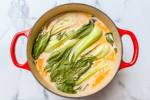 Cooked bok choy on top of curry soup in a large pot.
