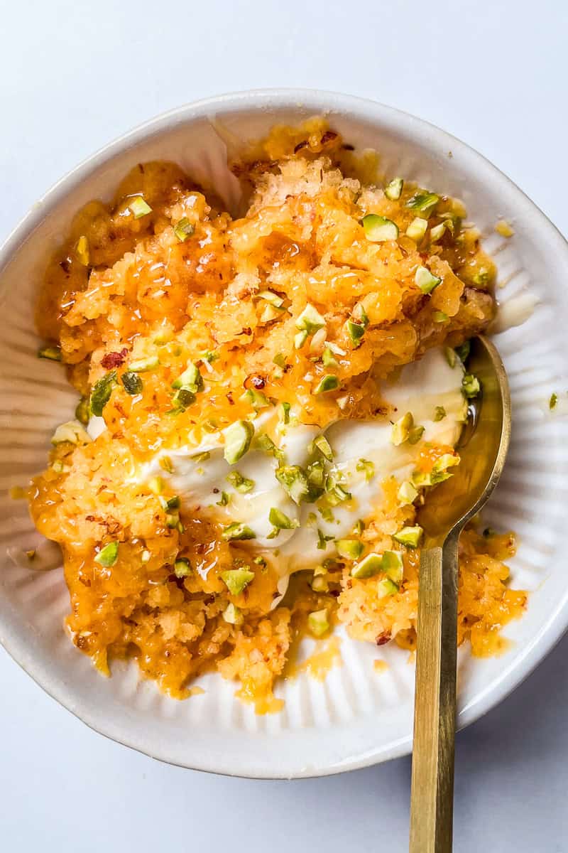 Shaved frozen peach with mascarpone, honey, and pistachios in a white bowl with a gold spoon.
