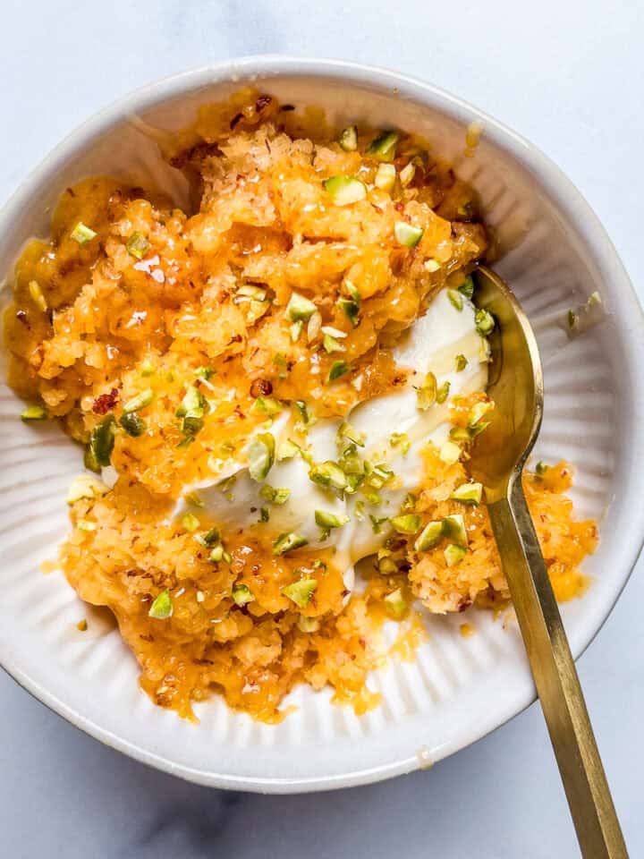 Shaved frozen peach with mascarpone, honey, and pistachios in a white bowl with a gold spoon.