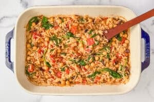 Mediterranean chickpea orzo bake with spinach and tomatoes in a baking dish.
