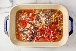 Canned tomatoes, orzo, chickpeas, diced olives, crumbled feta, spices, and vegetable stock in a baking dish.