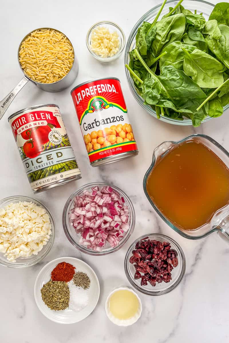 Ingredients for one pan Mediterranean orzo bake on a marble background.