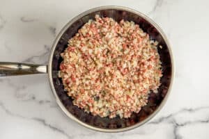 Pancetta, onions, and garlic cooking in a frying pan.
