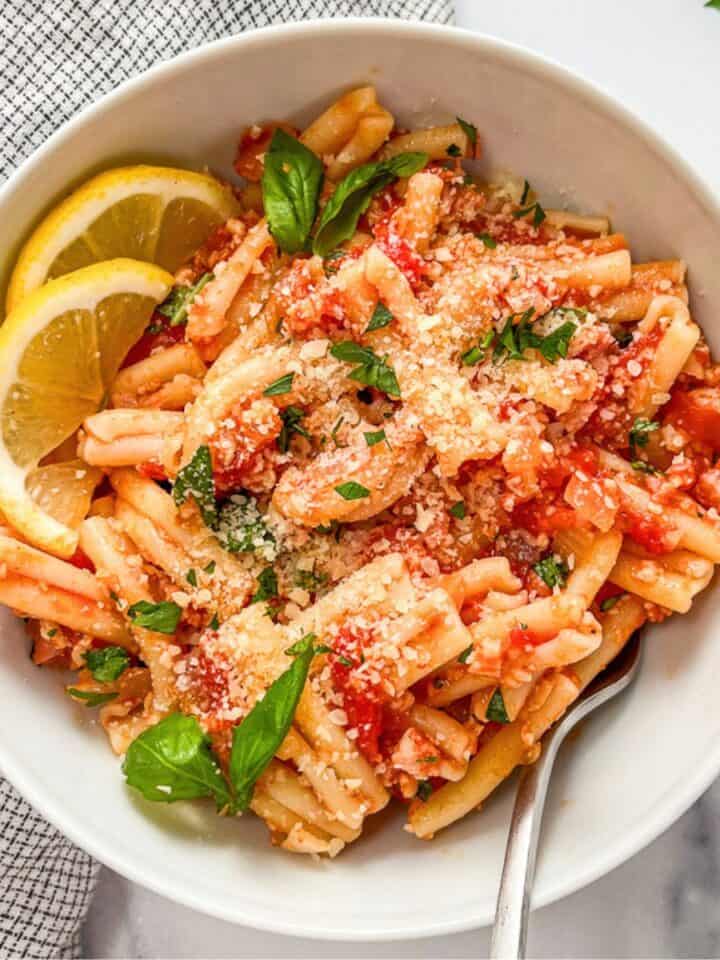 Tomato pasta with pancetta in a white bowl.