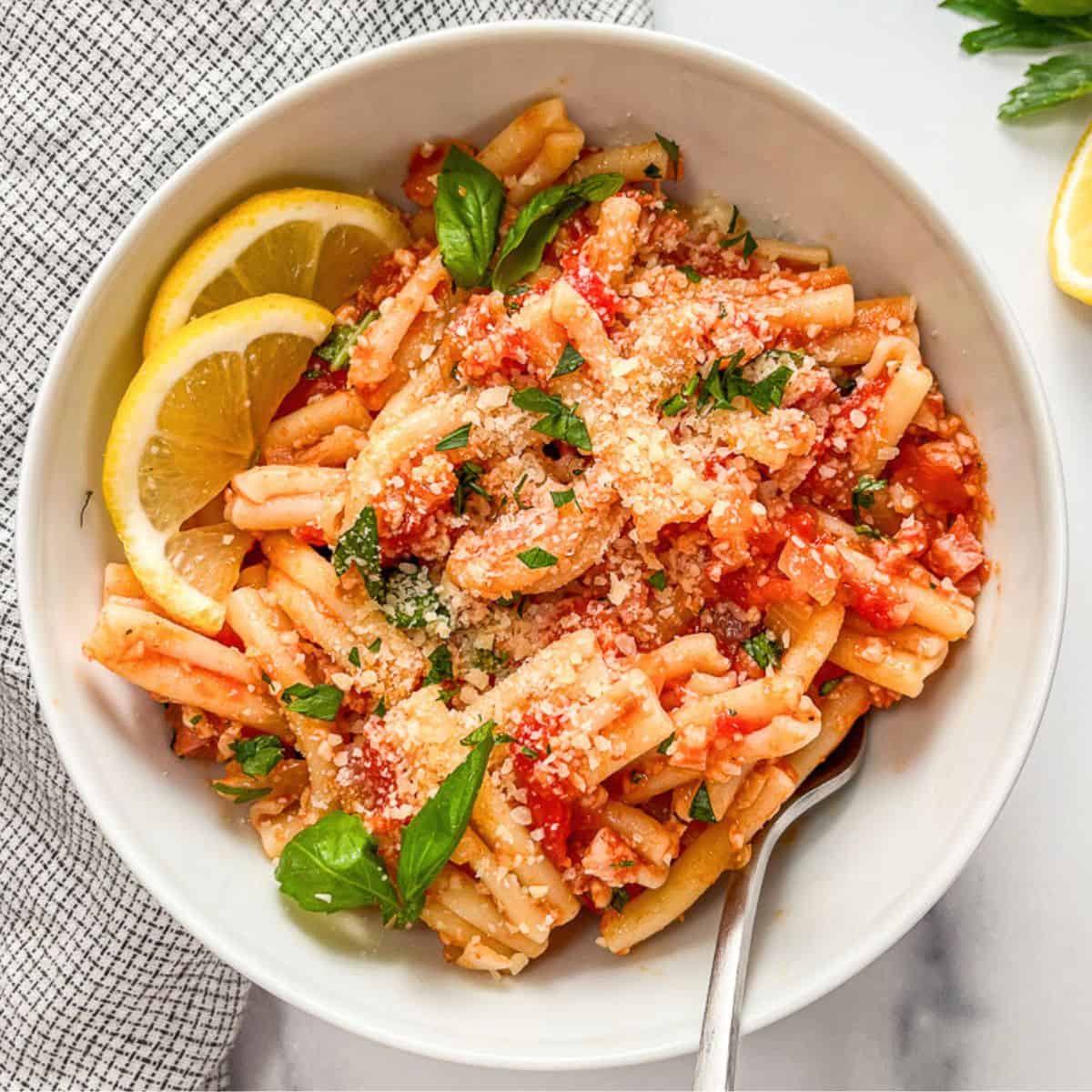 Tomato pasta with pancetta in a white bowl.