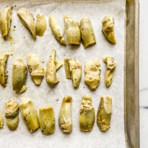 Artichoke hearts tossed with oil, salt, and pepper on a parchment lined sheet pan.