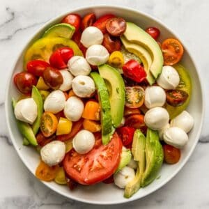 Tomatoes, avocado, and mozzarella balls in a large white bowl.