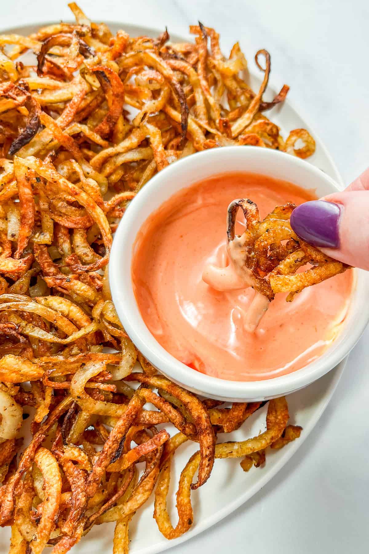 A baked curly fry being dipped into mayochup.