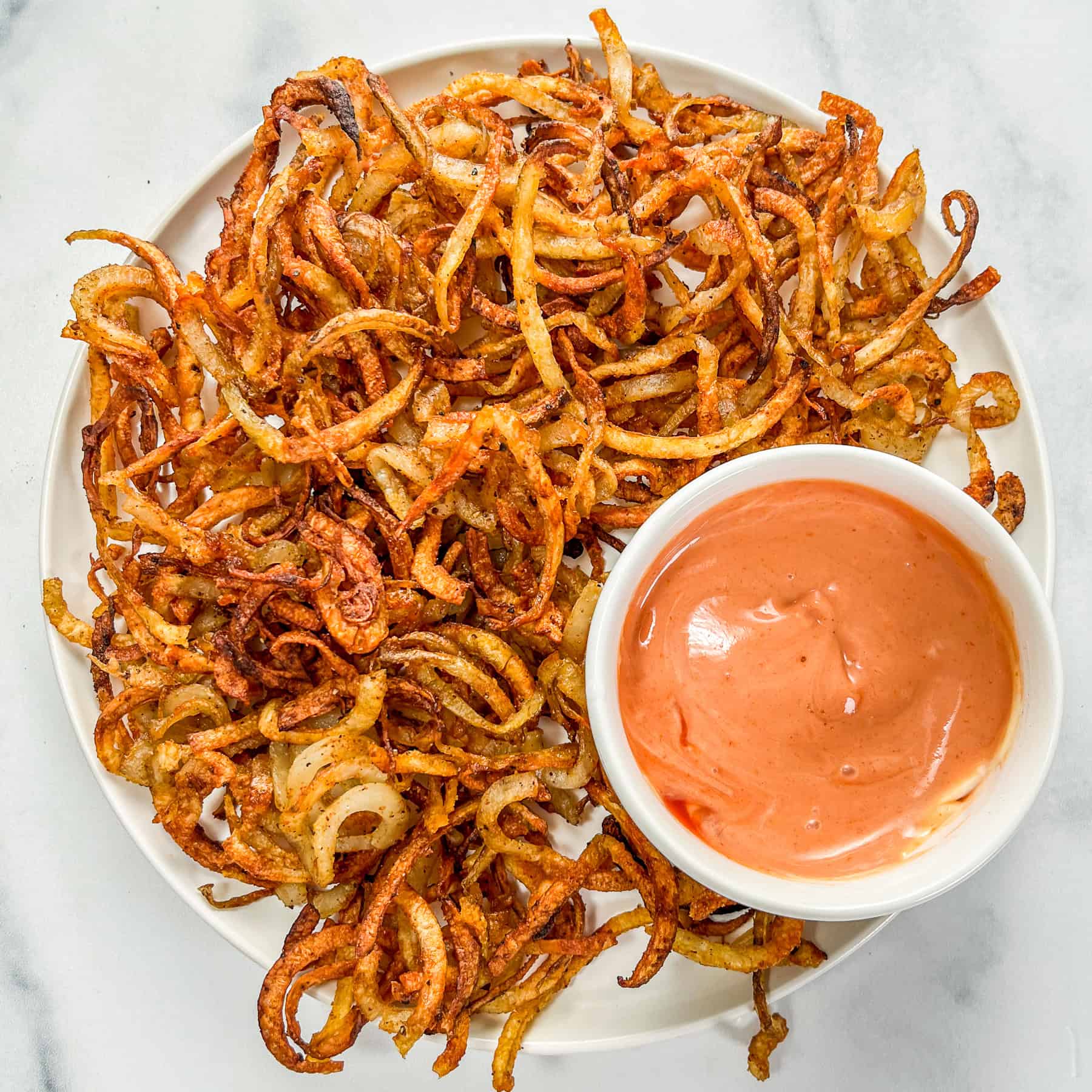 A plate of baked curly fries with a bowl of mayo and ketchup mixed together.