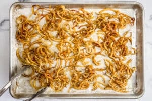 Half baked curly fries on a sheet pan being tossed with tongs.