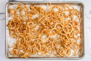 Spiralized pieces of potato tossed with spices on a parchment lined sheet pan.
