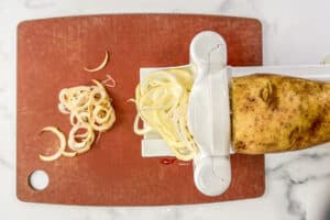 A potato being spiralized onto a brown cuttting board.