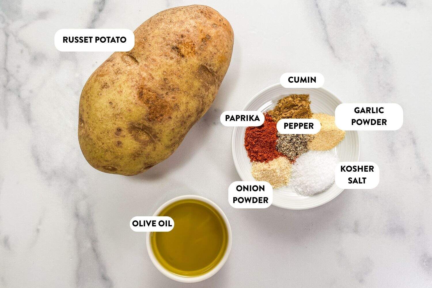 A potato, plate of spices, and olive oil on a marble background.