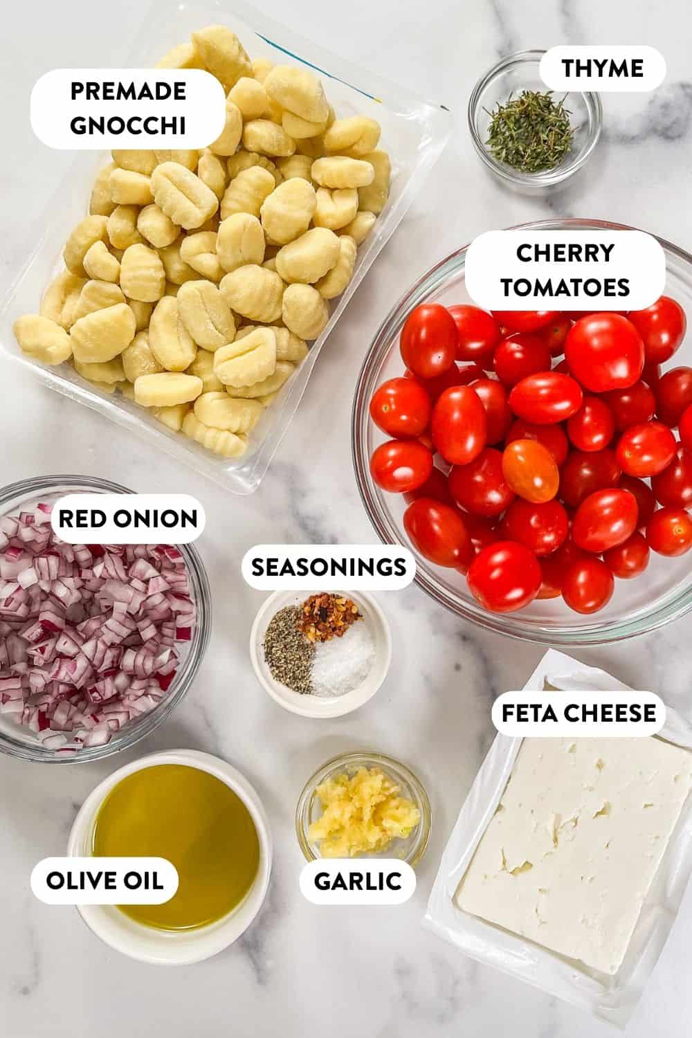 Ingredients for baked feta gnocchi on a marble background.