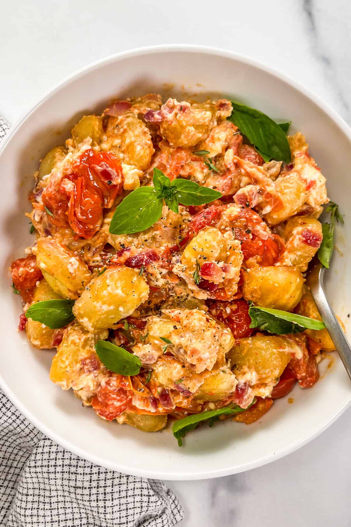 Baked feta gnocchi with tomatoes in a white bowl with a silver fork.