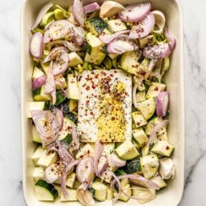 Zucchini, leek, feta, and shallots topped with olive oil and spices in a baking dish.