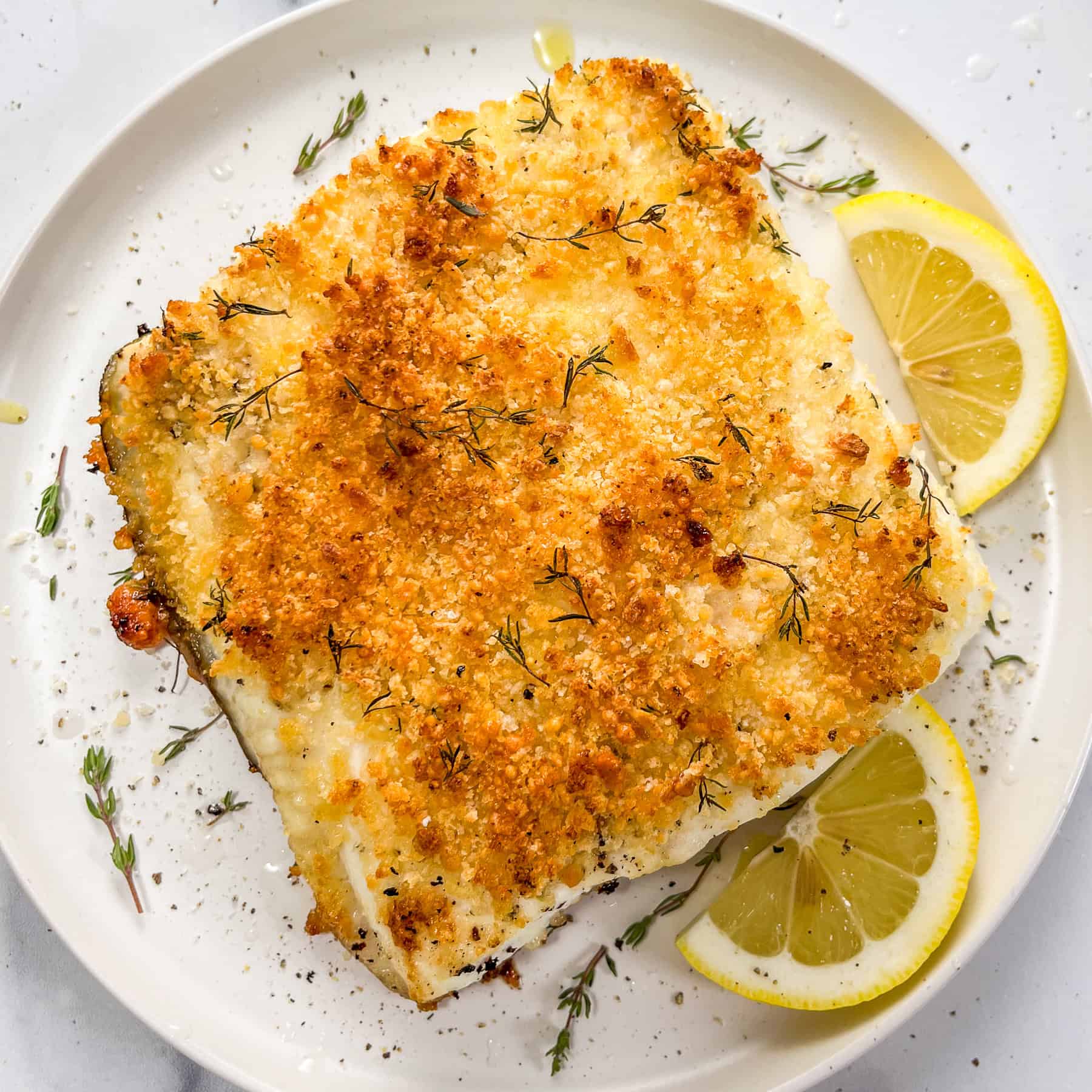 Baked parmesan panko halibut on a white plate with slices of lemon.