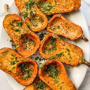 Miso roasted honeynut squash topped with parsley and sesame seeds on a white platter.