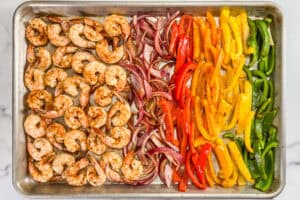 Baked green, yellow, orange, and red bell peppers, red onions, and shrimp on a sheet pan.
