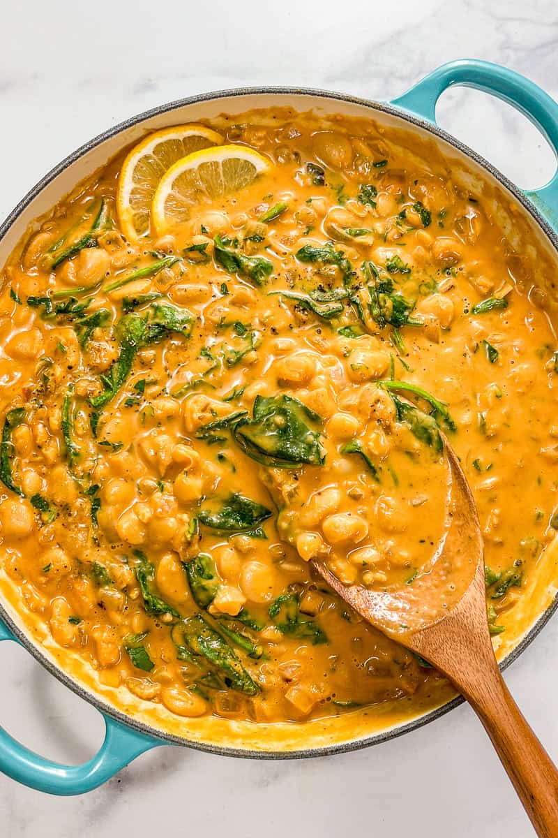 Creamy pumpkin butter beans with spinach in a pot with a wooden spoon.