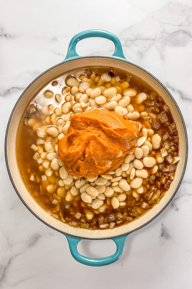 Vegetable broth, butter beans, and onions topped with pumpkin puree in a teal handled pot.