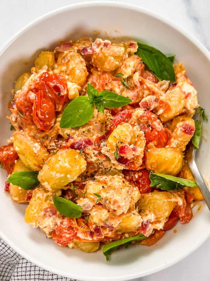 Baked feta gnocchi with cherry tomatoes and basil in a white bowl with a fork.