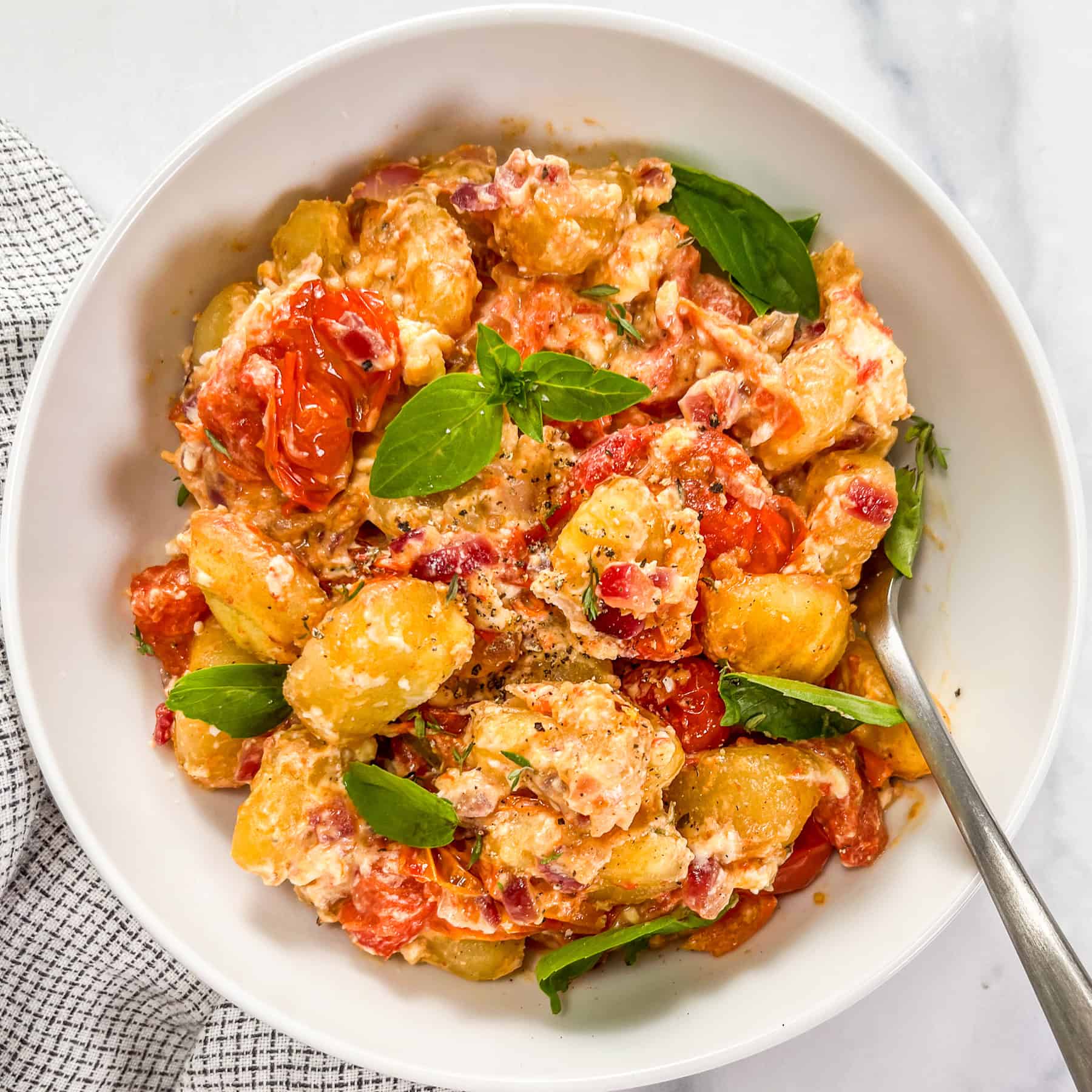 Baked feta gnocchi with cherry tomatoes and basil in a white bowl with a fork.