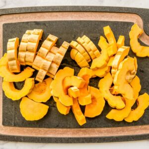 Sliced of delicata squash on a black cutting board.