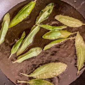 Sage leaves frying in oil in a pan.
