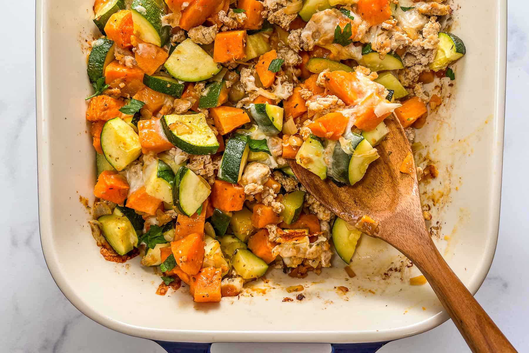 Ground turkey sweet potato bake with zucchini and mozzarella being scooped up with a wooden spoon.