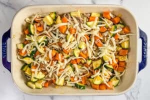 Ground turkey, sweet potatoes, and zucchini topped with shredded mozzarella cheese in a blue handled baking dish.
