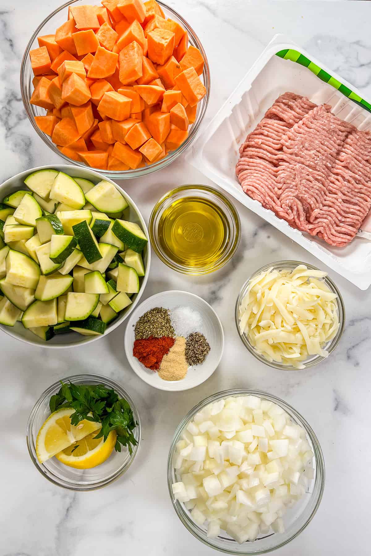 Ingredients for a ground turkey sweet potato bake on a marble background.