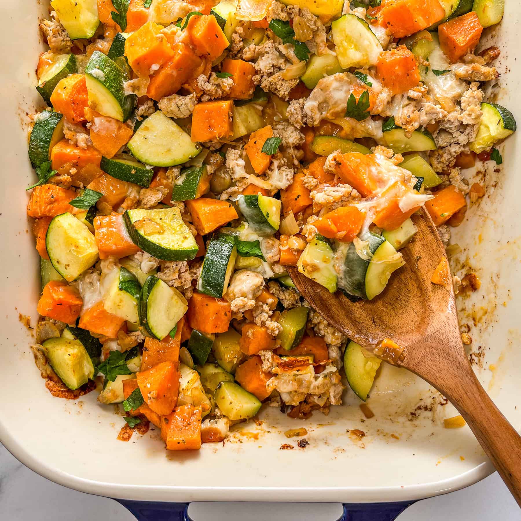 Sweet potato and zucchini ground turkey bake in a large baking dish with a wooden spoon.