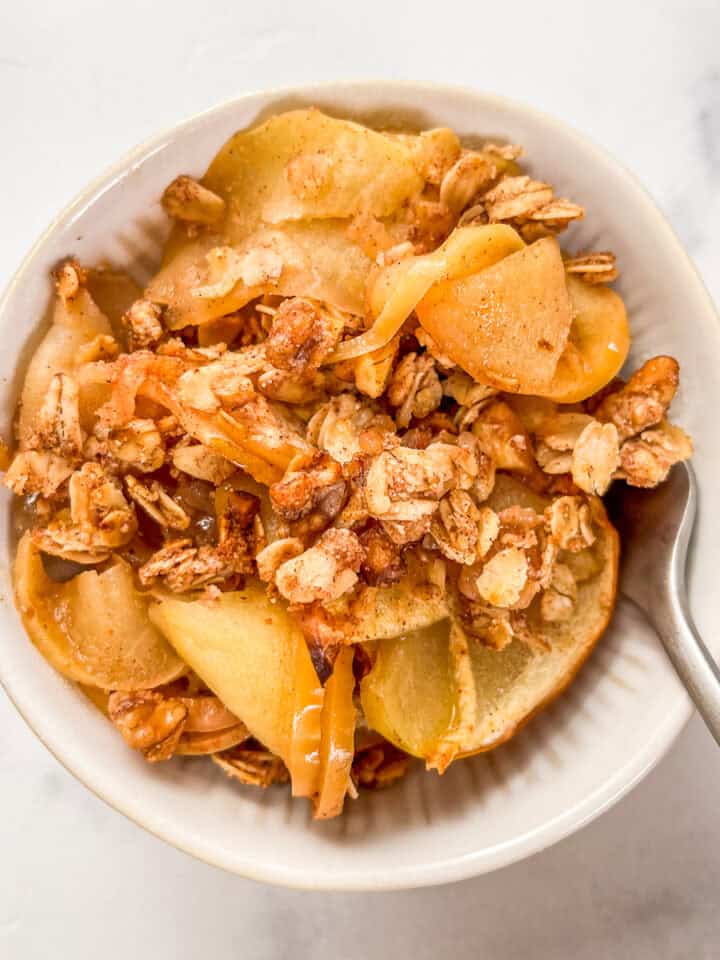 Healthy apple crisp in a white bowl with a silver fork.