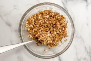 Apple crisp topping being stirred in a glass bowl with a spoon.