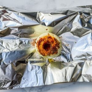 A cored onion covered in spices on a piece of aluminum foil.