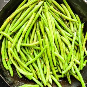 Green beans cooking with red pepper flakes in a skillet.