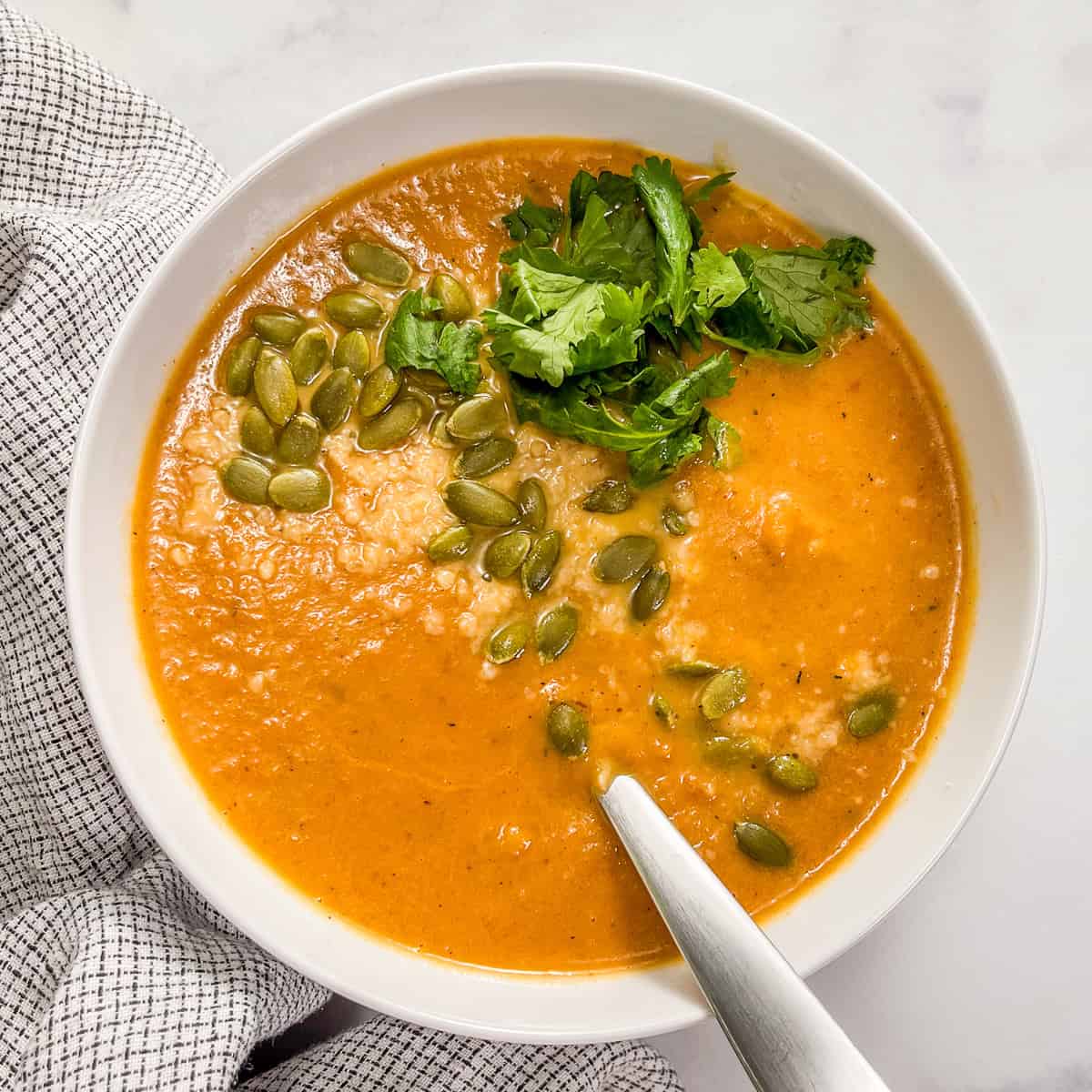 Marry me butternut squash soup topped with pepitas and parsley in a white bowl with a silver spoon.